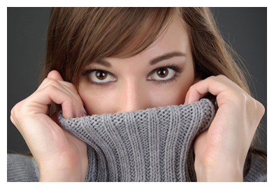A woman hides part of her face behind her gray turtleneck sweater.